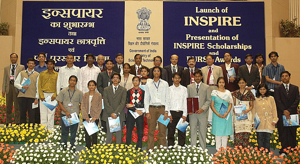 A group of people standing in an auditorium with some of them holding Inspire scholarship certificates in their hands